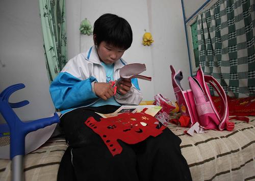 放學(xué)回到板房里的張春梅,坐在床邊做著剪紙作業(yè)(4月29日攝)。