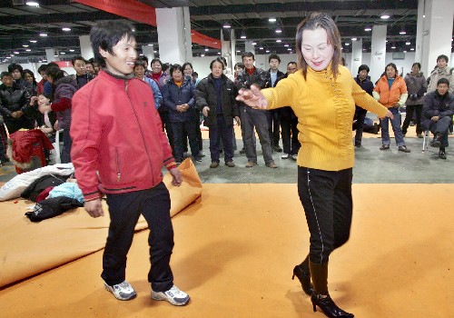 1月30日,在浙江農(nóng)展館臨時(shí)駐留點(diǎn),一名滯留旅客跟前來慰問演出的街道藝術(shù)團(tuán)演員學(xué)跳舞。新華社發(fā)(李忠 攝)
