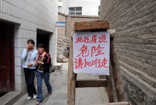 5月13日,在甘肅省隴南市武都區(qū),兩名行人走過一處因地震受損房屋旁邊的警示牌。