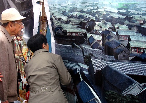 5月2日,兩位游客透過臨時(shí)圍墻招貼畫的縫隙,觀看前門大街街景。 新華社記者 王頌 攝