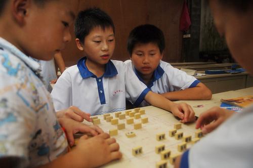幾名留守孩子在下軍棋(8月5日攝)。對(duì)于大多數(shù)孩子,暑假是豐富多彩的;而對(duì)農(nóng)村的不少留守孩子,暑假仍然無法跟父母團(tuán)聚,不得不繼續(xù)過著留守生活。在安徽涇縣王直留守兒童助教中心,暑期仍有80多名留守兒童在這里托管生活學(xué)習(xí)。由于缺少父母的陪伴,孩子們?cè)谥讨行睦蠋煹呐惆橄?,與同學(xué)們共同生活,開展文體活動(dòng)、復(fù)習(xí)功課。新華社記者 李健 攝