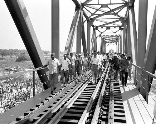 1974年9月18日,贊比亞總統(tǒng)卡翁達(dá)等官員視察坦贊鐵路謙比西河大橋。 1965年2月,坦桑尼亞總統(tǒng)尼雷爾訪華。劉少奇主席和周恩來總理在與尼雷爾總統(tǒng)會(huì)談時(shí)表示:中國政府同意幫助修建一條由坦桑尼亞到贊比亞的鐵路。1967年9月5日,中國、坦桑尼亞、贊比亞三國政府在北京簽訂《關(guān)于修建坦桑尼亞——贊比亞鐵路的協(xié)定》。在修建坦贊鐵路過程中,中國共有60余人長眠在了坦贊大地上。經(jīng)過5年多的艱苦努力,坦贊鐵路于1975年10月試辦運(yùn)營,1976年5月完成了全線工程收尾和設(shè)備安裝配套等工作。“鋼鐵斑馬”終于馳騁在千里莽原上。贊比亞總統(tǒng)卡翁達(dá)說:坦贊鐵路是“我們與中國友誼和團(tuán)結(jié)的紀(jì)念碑。”坦贊鐵路東起坦桑尼亞首都達(dá)累斯薩拉姆,西至贊比亞中央省的卡皮里姆博希,與贊比亞原有鐵路接軌,全長1860.5公里,是一條貫通東非和中南非的大干線,極大地改善了坦、贊兩國的交通運(yùn)輸狀況。新華社發(fā)