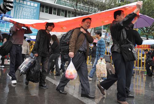 2月7日,在廣州火車站前,幾名旅客舉著遮雨布行進(jìn)。新華社記者 盧漢欣 攝