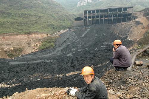兩名工人蹲在錳渣庫旁,遠處建筑為排放錳渣的壓力車間(4月11日攝)。新華社記者范軍威 攝