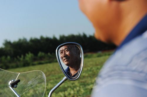 曾經(jīng)開船的移民匡永見開著摩托車查看草莓育苗情況(8月4日攝)。新華社記者 李健 攝