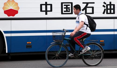 7月9日,一名學(xué)生騎車從北京街頭印有“中國石油”標(biāo)志的大巴車前經(jīng)過。新華社記者 王建華 攝
