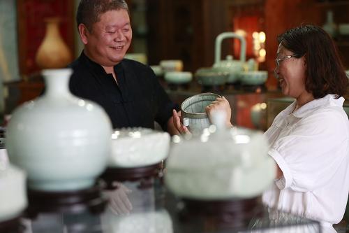 8月14日,在遼寧省西部的朝陽市喀左縣,從浙江龍泉北上創(chuàng)業(yè)的國家級工藝美術(shù)師周明亮(左)向一位顧客介紹其研發(fā)制作的遼青瓷作品。新華社記者 任正來 攝