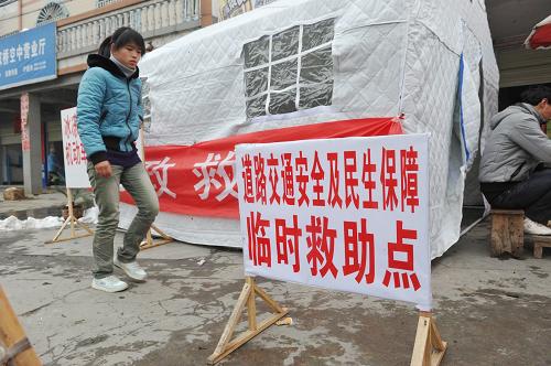 1月23日,在貴州玉屏侗族自治縣,一居民從“臨時救助點”前經(jīng)過。玉屏縣目前已準備12個“臨時救助點”,隨時準備安置因凝凍而滯留的旅客。新華社記者 歐東衢 攝