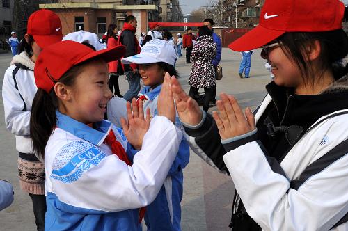3月5日,在濟(jì)南市文苑小學(xué),山東大學(xué)青年志愿者劉潔冰(右)和在此就讀的農(nóng)民工子女蕭涵一起玩游戲。新華社記者 徐速繪 攝
