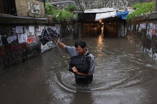 6月10日,一名當(dāng)?shù)鼐用裉仕ㄟ^湖南省婁底市新火車站附近積水的通道。新華社發(fā)(郭國權(quán) 攝)