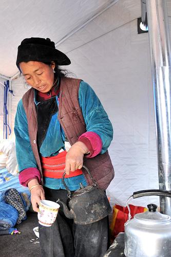 2月12日,受災(zāi)村民包王加村在黑多村的臨時安置點里煮奶茶。新華社記者 陳斌 攝