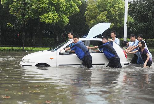 7月5日,江蘇揚(yáng)州街頭的積水中,志愿者幫忙推動(dòng)熄火的車輛前行。新華社發(fā)(程建平 攝)