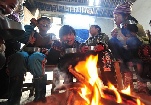 1月6日,在廣西馬山縣白山鎮(zhèn)民新小學(xué),學(xué)生們一邊烤火,一邊享用免費(fèi)午餐。新華社記者 黃孝邦 攝