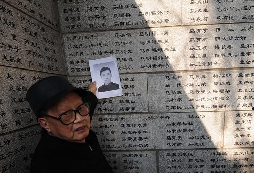 4月4日,南京大屠殺幸存者向遠(yuǎn)松帶著遇難哥哥向遠(yuǎn)高的遺像,在遇難者名單墻前祭奠。新華社記者 孫參 攝