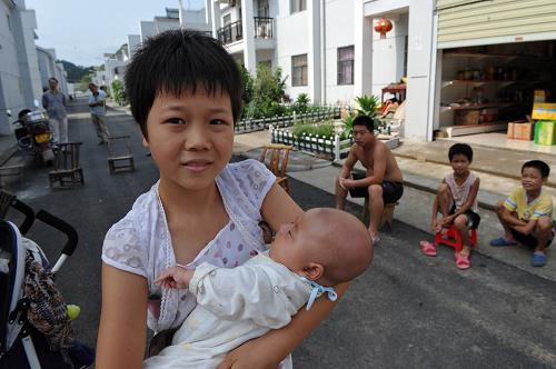 湖北省鄖縣臥龍崗移民安置點11歲的小移民肖秋萍在家門口幫大人帶孩子(7月29日攝)。新華社記者 郝同前 攝