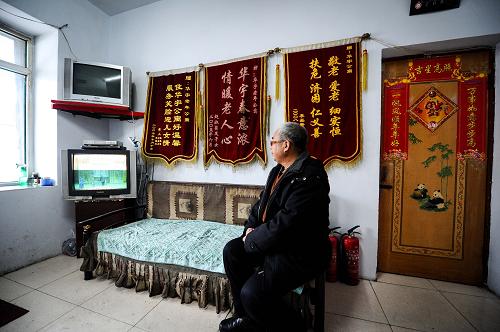 長春在華宇老年公寓工作人員張亞軍在看電視解悶,身后墻上掛滿了院內(nèi)老人及家屬所贈與的錦旗(1月16日攝)。今年67歲的張亞軍是華宇老年公寓內(nèi)的工作人員,也算是半個護工,在接待來訪者的空閑時,幫忙照顧院內(nèi)的20多位老人。新華社記者 許暢 攝