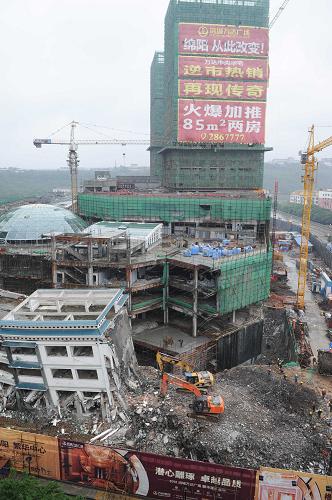 5月21日,工程機(jī)械在拆除綿陽紫荊民族中學(xué)校舍,旁邊則是建設(shè)中的萬達(dá)廣場。新華社記者 李橋橋 攝