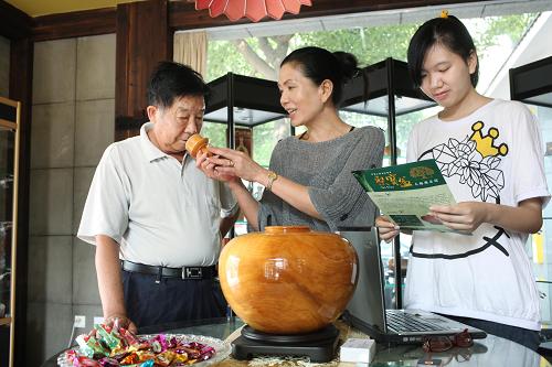 6月21日,店主陳金卿(中)請顧客(左)品鑒臺灣木雕工藝品——檜木聚寶盆。新華社發(fā)(丁煥新 攝)