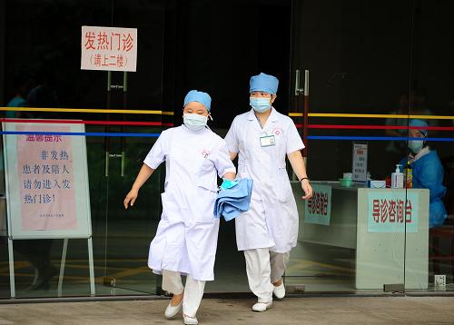 6月22日,兩名醫(yī)護(hù)人員走出東莞市石龍人民醫(yī)院發(fā)熱門診,這里收治了12名石排鎮(zhèn)中心小學(xué)學(xué)生。 新華社記者 陳曄華 攝