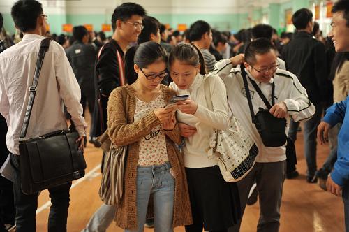 10月25日,兩名應聘學生在校園招聘會上查看用人單位的宣傳冊。新華社記者 周密 攝