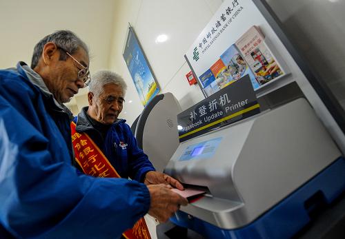 10月17日,72歲的養(yǎng)老金志愿者劉忠(右)協(xié)助一位老人使用網點內的補登折機。新華社記者 張宇 攝