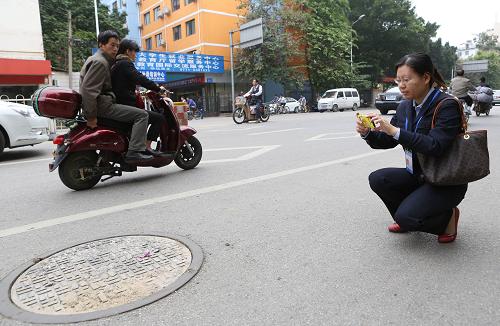 11月12日,廣西南寧市天桃小學大門前的慢車道上,城市管理監(jiān)督中心巡查員盧曉敏在拍攝蓋好蓋子的井口,隨后她通過手機上傳報告給監(jiān)督中心,井蓋遺失問題已經(jīng)解決。 新華社發(fā)(龍濤 攝)