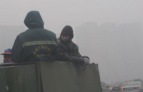1月15日,鄭州市的幾名環(huán)衛(wèi)工人乘施工車從街頭經(jīng)過。新華社記者 趙鵬 攝