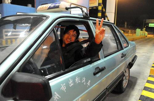 2月9日零時過后,一輛從上海返回?fù)P州的出租車成為啟揚高速揚州段揚州西收費站駛出的首輛免費通行小型客車,司機(jī)擺出“勝利”手勢。新華社發(fā)(莊文斌 攝)