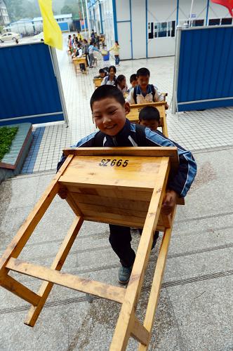 5月24日,四川省雅安市雨城區(qū)上里鎮(zhèn)中心學(xué)校的學(xué)生將課桌搬進加固后的綜合樓。新華社發(fā)(李向雨 攝)