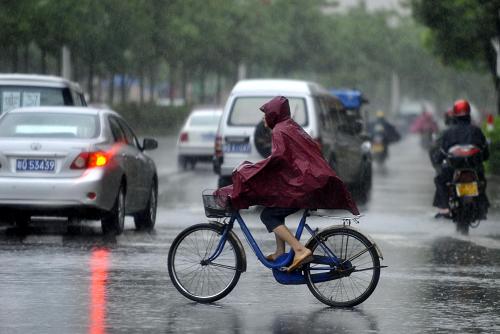 7月24日,在受臺風“韋森特”影響的廣東陽江街頭,市民穿著雨衣騎行過馬路。新華社記者 陳曄華 攝