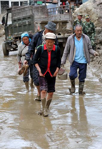 8月7日,云南省洱源縣鳳羽鎮(zhèn)鐵甲村的一些村民趟過(guò)泥水路面準(zhǔn)備回家收拾東西。新華社記者 藺以光 攝