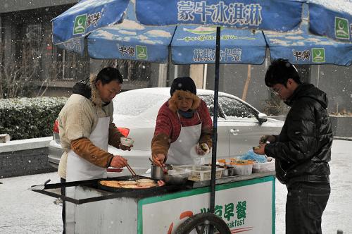 北京出現(xiàn)降雪天氣 12月12日,經(jīng)營(yíng)早餐攤點(diǎn)的商販在雪中為顧客服務(wù)。 當(dāng)日早晨,北京出現(xiàn)較大范圍降雪天氣。 新華社記者 孫瑞博 攝