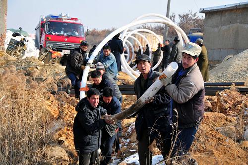 1月12日,在山東乳山唐家溝金礦救援現(xiàn)場,當?shù)厝罕姾途仍藛T一起鋪設排水管進行救援。新華社發(fā)