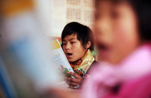 12月17日,在會寧縣北關小學讀書的藏族學生班馬仲格(左)在語文課上讀書。甘肅省會寧縣的中小學校里,有123名來自千里之外的甘南藏族自治州瑪曲縣的藏族中小學生就讀。他們能夠在會寧接受優(yōu)質教育,受益于會寧與瑪曲之間的一項教育幫扶協(xié)議。會寧縣是西北教育大縣和甘肅省的“狀元縣”,恢復高考制度以來,先后為國內各大專院校培養(yǎng)了5萬名優(yōu)秀畢業(yè)生。在甘肅相關部門和甘南宗教界人士的推動下,會寧縣與瑪曲縣就教育幫扶達成協(xié)議,從2004年秋季起,15年內,瑪曲每年向會寧輸送20名藏族學生,在會寧接受從小學到高中的教育?,斍h教育部門介紹,這個計劃實施5年以來,孩子們的學習成績和各方面素質有明顯提高。為了給藏族孩子提供便利,會寧縣不僅不收取費用,還向他們發(fā)放食宿補貼?,斍h則專門派出了生活老師和藏語老師,照料孩子們的生活,并教授他們藏語。走出草原的藏族孩子開闊了眼界,增長了才干?,斍h教育局帶隊老師扎西才讓說:“經(jīng)過在會寧的苦讀,這些孩子中肯定會出不少人才,他們將成為草原建設的棟梁。”