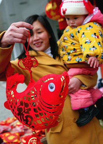 2月13日,在廣西融水苗族自治縣縣城,一名母親抱著孩子選購春節(jié)裝飾品。新華社發(fā)(龍濤 攝)