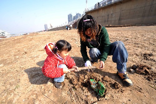 12月6日,參加清污活動的一位母親帶著孩子在湘江裸露的河床上挖出被深埋的垃圾。新華社記者 趙眾志 攝