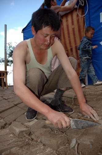 隴南市武都區(qū)馬街鎮(zhèn)姜家山村村民把從廢墟中清理出的磚頭暫時鋪在帳篷前硬化路面(6月10日攝)。新華社記者 宋常青 攝