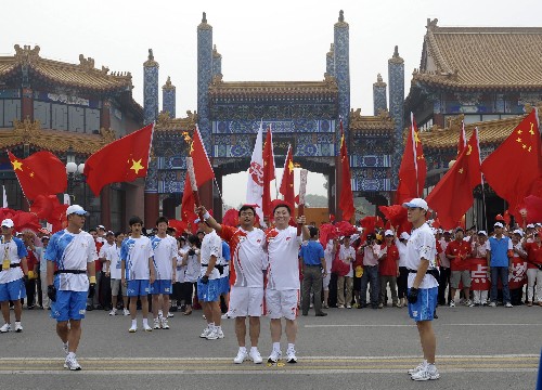 8月7日,火炬手關(guān)成華(右)與下一棒火炬手黃福水交接火炬后慶祝。當(dāng)日,北京奧運(yùn)圣火在北京市傳遞。 新華社記者戚恒攝