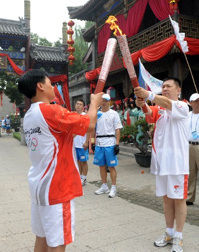 8月7日,火炬手韓金榮(右)與下一棒任曉云交接。當(dāng)日,北京奧運(yùn)圣火在北京市傳遞。 新華社記者劉力航攝
