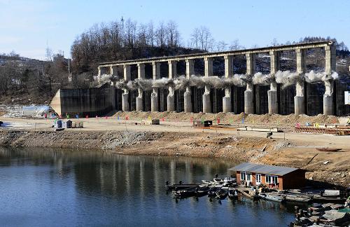 12月28日,施工人員對(duì)水豐水電站副壩工作橋進(jìn)行爆破拆除。當(dāng)日11時(shí)許,鴨綠江上第一座電站——水豐水電站防洪設(shè)施改造工程副壩1至12號(hào)工作橋及13個(gè)橋墩成功啟爆,并按預(yù)期傾覆至副壩上游庫(kù)區(qū)。根據(jù)中國(guó)和朝鮮兩國(guó)政府協(xié)定,鴨綠江上四座水電站由中朝水力發(fā)電公司理事會(huì)負(fù)責(zé)管理(中方理事會(huì)設(shè)在國(guó)家電網(wǎng)公司),其中水豐水電站由朝方管理。水豐水電站是鴨綠江上第一座電站,已運(yùn)行近70年,設(shè)備十分老舊,大壩、防洪和發(fā)電等設(shè)備存在嚴(yán)重安全隱患。2009年2月,中朝雙方形成了水豐大壩防洪設(shè)施改造工程具體實(shí)施方案的決議。2009年8月15日,工程正式開(kāi)工。本次改造工程由東北電網(wǎng)公司負(fù)責(zé),其工程的施工組織管理委托太平灣發(fā)電廠負(fù)責(zé),計(jì)劃工期為三年。水豐水電站副壩壩頂全長(zhǎng)273米,設(shè)有18個(gè)溢流門(mén)。本次改造需要對(duì)壩頂工作橋及橋墩進(jìn)行拆除,2009年8月至2010年7月,已完成了6孔工作橋及閘門(mén)的改造工作。本次副壩工作橋定向控制爆破拆除取得圓滿成功,將大大縮短副壩混凝土拆除工期,為保證副壩2011年6月30日前具備防洪能力創(chuàng)造了有利條件。新華社記者 任勇 攝