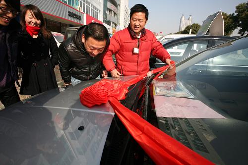 12月29日,在江蘇省泰州市一家汽車銷售公司,一市民看著新買的小排量車掛上紅綢帶開心不已。新華社發(fā)(顧俊 攝)
