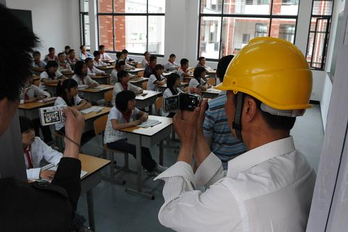 5月9日,兩名援建工人正在拍攝剛搬進(jìn)新校舍上第一堂課的學(xué)生們。新華社記者 楊磊 攝