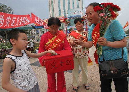 5月16日,陜西省咸陽市擁軍模范、“山丹丹擁軍之家”創(chuàng)辦人張娟娟(右一)和志愿者一起在咸陽市人民廣場上義賣鮮花,幫助地震災(zāi)區(qū)。一位小朋友將錢投入款箱中。 從5月15日開始,張娟娟就和“擁軍之家”的志愿者一道在街頭義賣鮮花,并將義賣所得寄給中國紅十字總會。 新華社發(fā)(何建虎 攝)