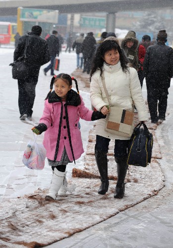 1月27日,一對(duì)即將檢票進(jìn)站的母女從蘭州火車站站前廣場(chǎng)鋪設(shè)的防滑毯上走過(guò)。 新華社記者 韓傳號(hào) 攝