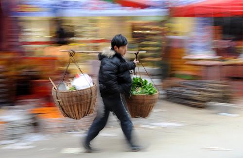 1月30日,湖北省宣恩縣一名菜農(nóng)挑著擔(dān)子上街賣(mài)菜。新華社發(fā)(宋文 攝)