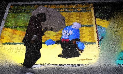 4月26日,在上海世博園浦東園區(qū),參觀者打傘的身影和大屏幕的海寶形象倒映在地面上的積水里。當(dāng)日,上海世博園舉行第六場試運(yùn)行,不少參觀者在雨中游覽上海世博園。新華社記者 吳曉凌 攝