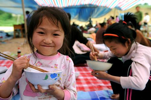2008年5月13日,在陜西省寧強縣青木川鎮(zhèn)輔仁中學避震點,兩名小女孩在吃午餐。 新華社發(fā)