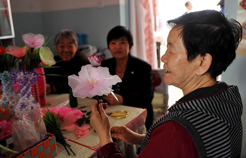 在烏魯木齊市水磨溝區(qū)長(zhǎng)青四隊(duì)南湖馨苑小區(qū)的居家托老所內(nèi),王傳梅老人(右)在制作手工藝編織花卉(9月23日攝)。新華社記者 王菲 攝