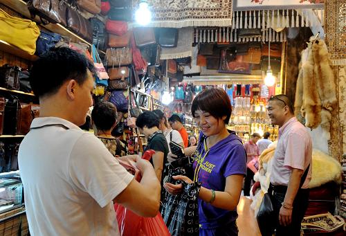 一名來(lái)自武漢的游客(前左二)在新疆國(guó)際大巴扎購(gòu)買(mǎi)商品(7月4日攝)。7月的烏魯木齊街頭瓜果飄香,又到了每年旅游最旺時(shí)節(jié)。新疆國(guó)際大巴扎人聲鼎沸,游客流連忘返。具有濃郁伊斯蘭建筑風(fēng)格的新疆國(guó)際大巴扎(維吾爾語(yǔ),意為集市)占地近4萬(wàn)平方米,是中亞最大的商品集散地,市場(chǎng)內(nèi)經(jīng)營(yíng)項(xiàng)目繁多,從手工藝品到玉器珠寶,從各類(lèi)干果水果到品牌服飾。新疆國(guó)際大巴扎總經(jīng)理烏什庫(kù)·尤努斯說(shuō),今年的旅游旺季來(lái)得比往年早,而且客流量增加,每天接待旅游團(tuán)50個(gè)左右,客流量達(dá)上萬(wàn)人次。新華社記者 王菲 攝