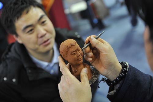 12月20日,一名參展藝術(shù)家在展覽現(xiàn)場(chǎng)為一名參觀者制作泥塑肖像。新華社記者 魯鵬 攝